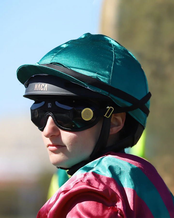 Jockey portant le casque de course NACA Comète S Racing MATE sous une toque de soie verte, lunettes de course