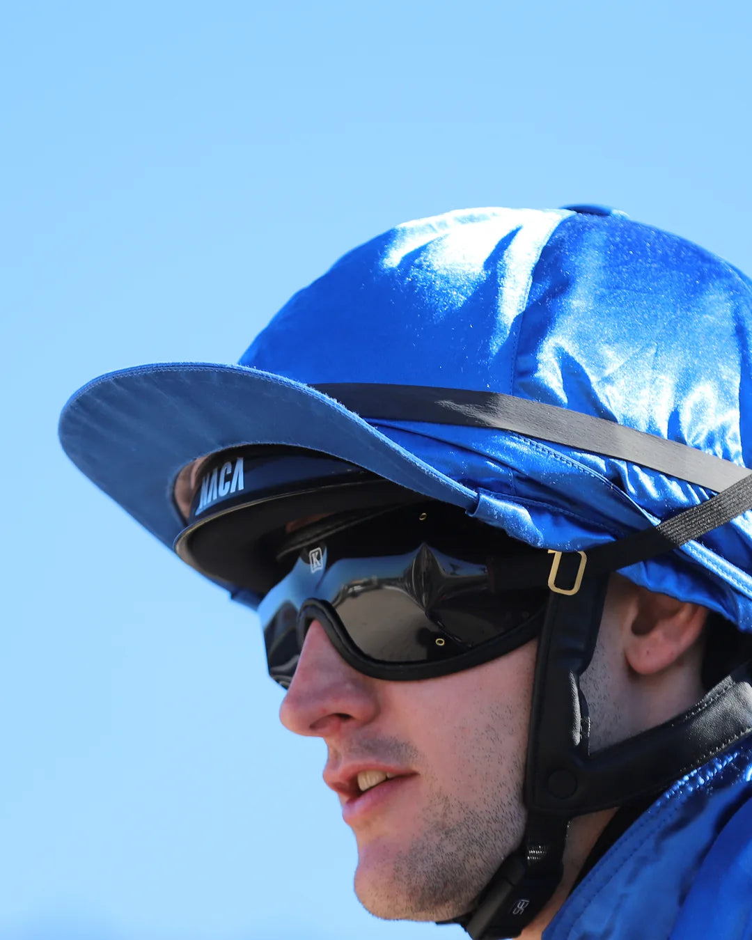 Gros plan sur le casque NACA COMÈTE S Racing Glow porté par le jockey Marvin Grandin sous sa toque bleue
